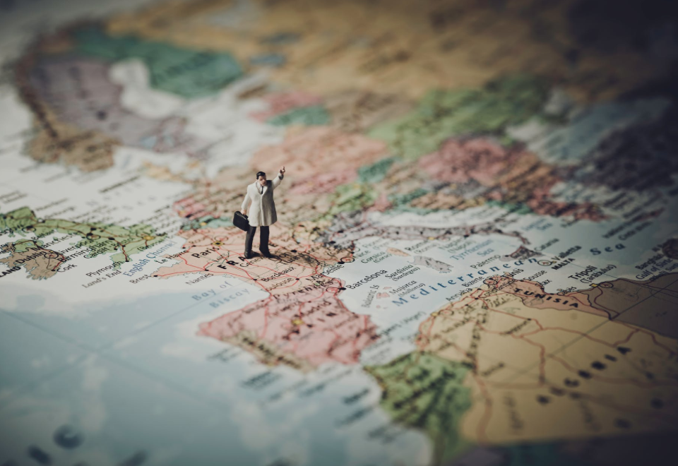 A small plastic figure dressed in a raincoat has his hand in the air on a map of Europe