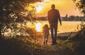 A father holds hands and leads his child towards a lovely sunset
