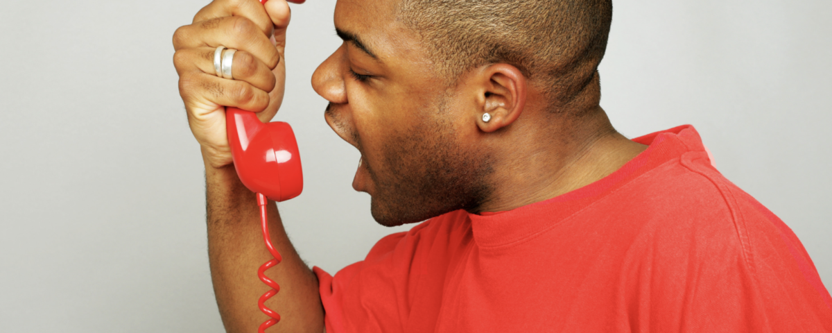 A man in a red tee-shirt shouts angrily into a telephone