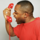 A man in a red tee-shirt shouts angrily into a telephone